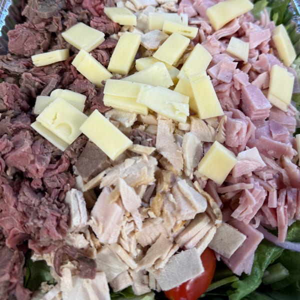 Close-up of a salad with diced ham, roast beef, chicken, and cheese cubes.