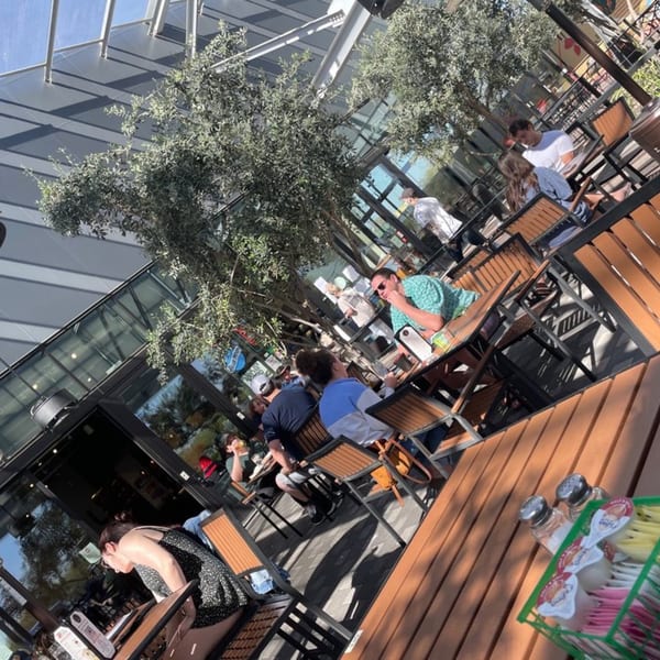 Patrons enjoying outdoor seating at New York Bagels 'N Bialys, with trees and modern architecture.