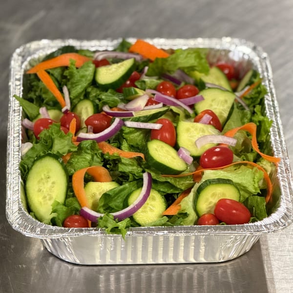 Fresh garden salad with lettuce, cucumbers, tomatoes, red onions, and carrots in a foil container.
