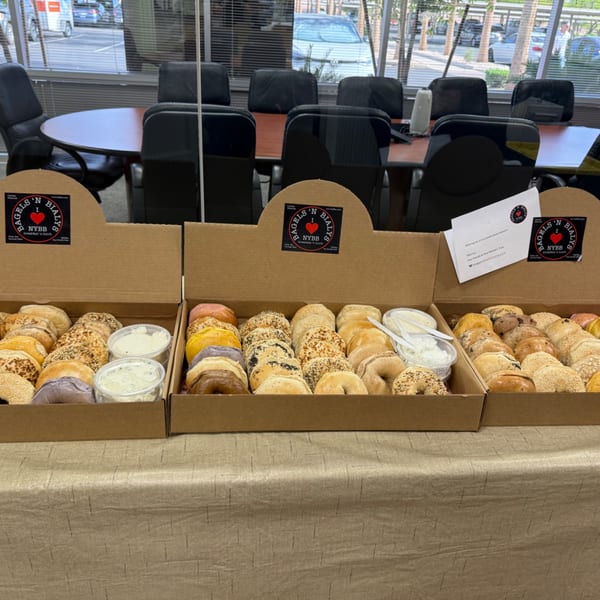 Three open boxes of assorted bagels and cream cheese from New York Bagels 'N Bialys on a table.
