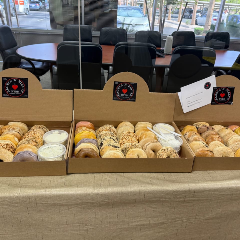 Three open boxes of assorted bagels and cream cheese from New York Bagels 'N Bialys on a table.