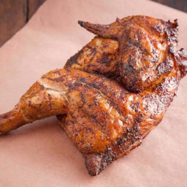 A large piece of roasted chicken with crispy, dark brown skin on a light brown surface.