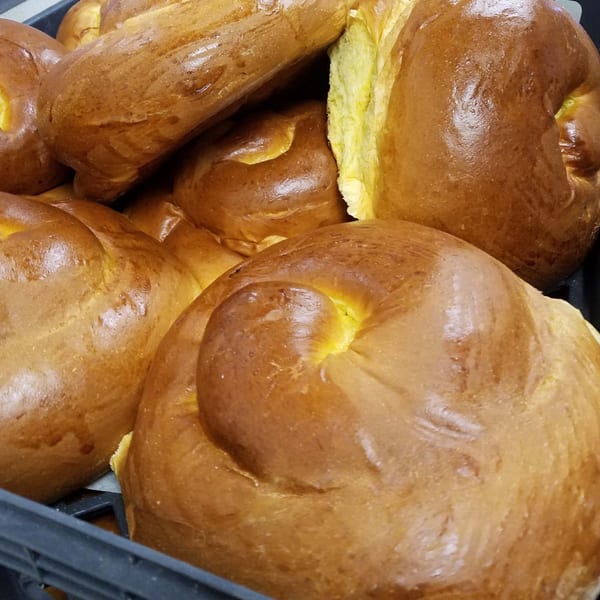 Close-up of several golden-brown challah loaves with visible yellow interiors, in a black basket.