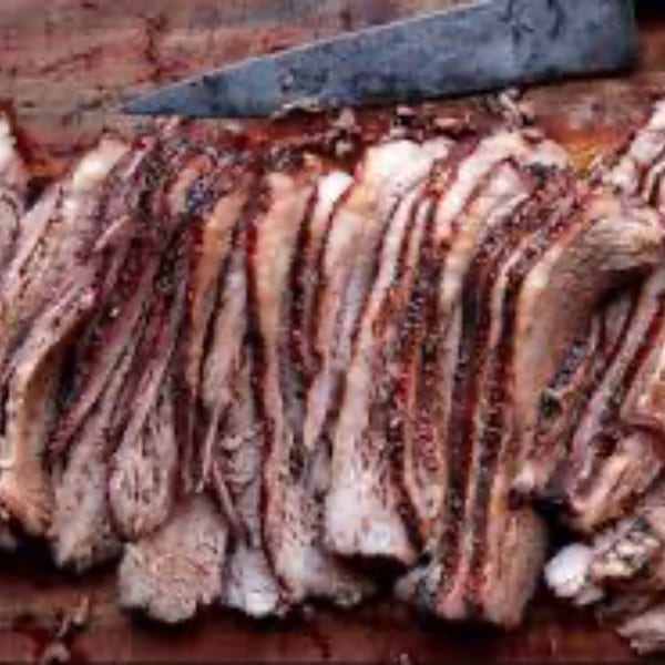 Thinly sliced pastrami with a knife resting on top, ready to be served.