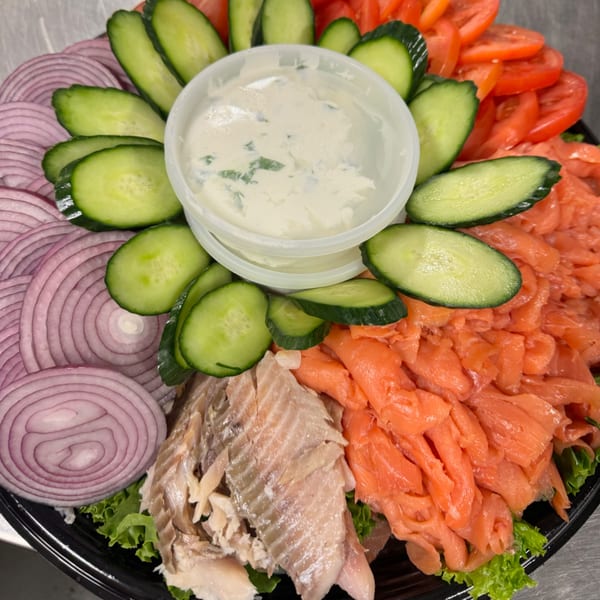 A platter of sliced red onions, cucumbers, tomatoes, lox, and whitefish salad.