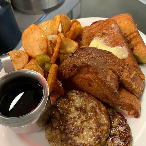A breakfast platter with French toast, sausage patties, home fries, and a side of syrup.