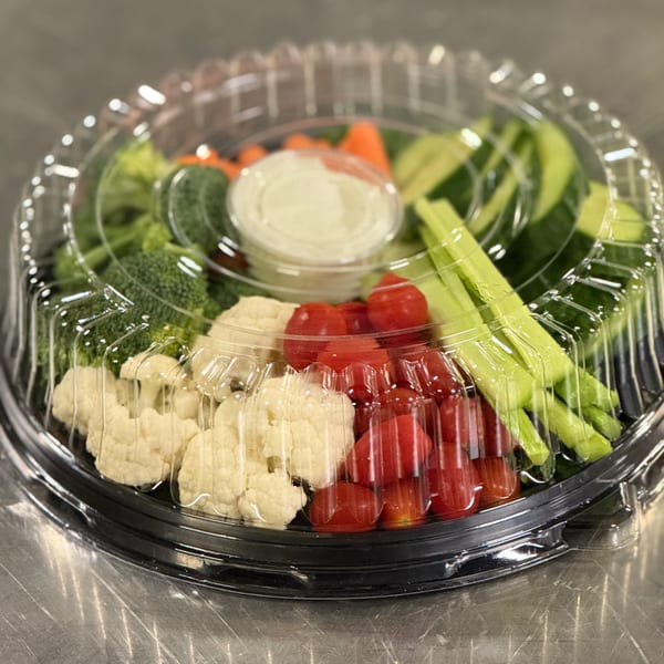 A plastic platter of fresh vegetables including broccoli, cauliflower, cherry tomatoes, celery, and carrots with dip.