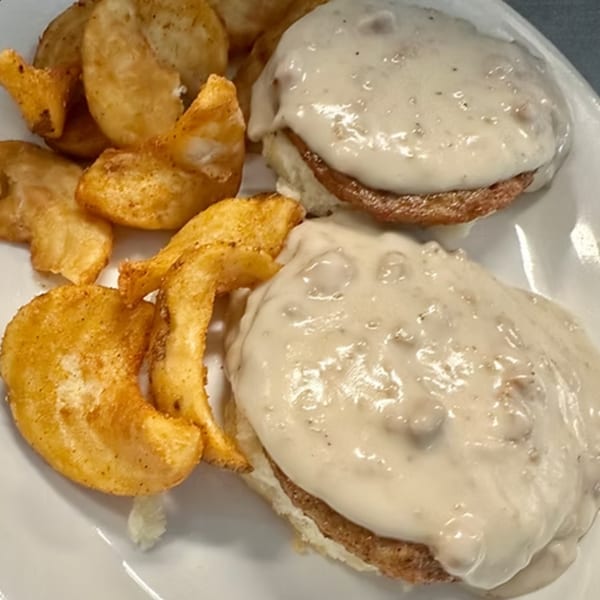 Biscuits and gravy with a side of seasoned potato wedges on a white plate.