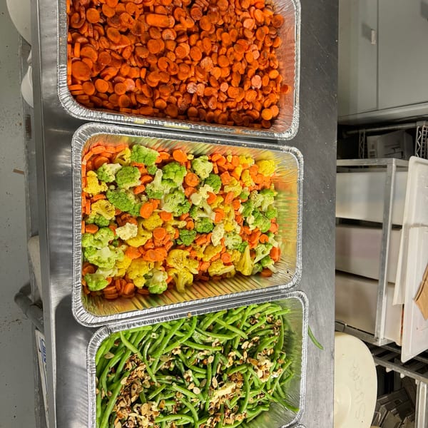 Three foil trays of cooked vegetables: carrots, mixed cauliflower and carrots, and green beans with almonds.