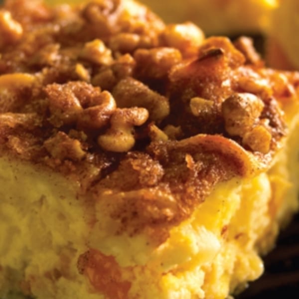 Close-up of a golden-brown baked good, possibly a bagel pudding, topped with nuts and cinnamon.