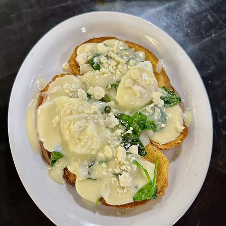Two pieces of toast topped with poached eggs, creamy sauce, spinach, and crumbled cheese.