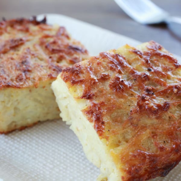 Two golden-brown squares of kugel, a traditional Jewish noodle pudding, on a white plate.