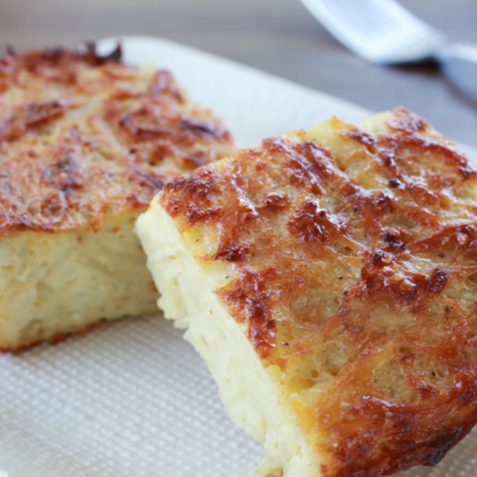 Two golden-brown squares of kugel, a traditional Jewish noodle pudding, on a white plate.