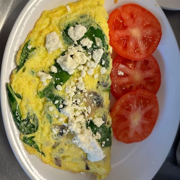 A fluffy omelet with spinach, mushrooms, and feta cheese, served with sliced tomatoes.