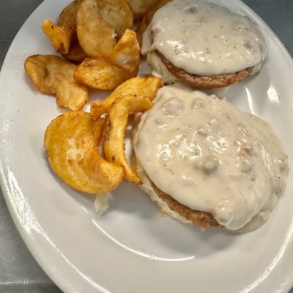 Two biscuits and gravy with a side of golden-brown potato wedges on a white plate.