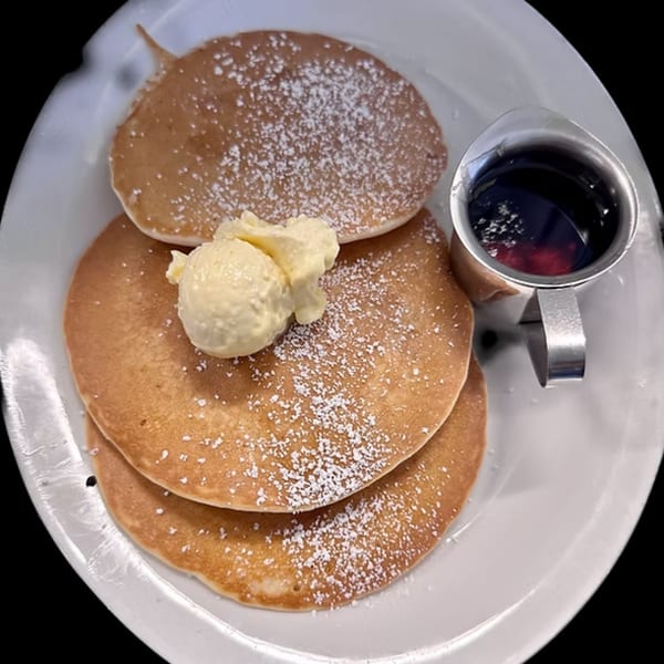 Stack of three pancakes with powdered sugar, a scoop of butter, and a side of syrup.