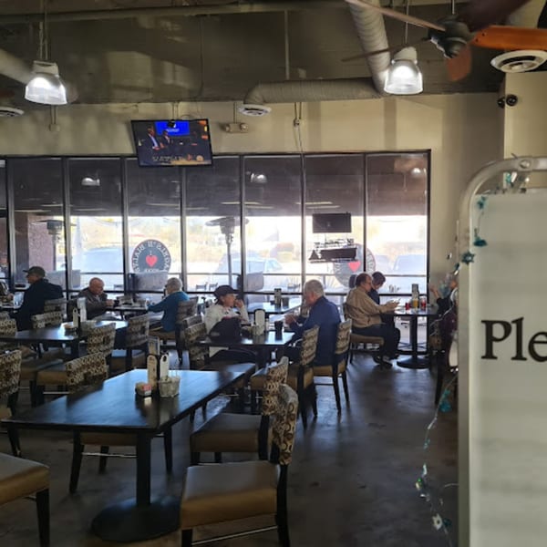 Diners seated at tables inside New York Bagels 'N Bialys, with large windows and a TV screen.