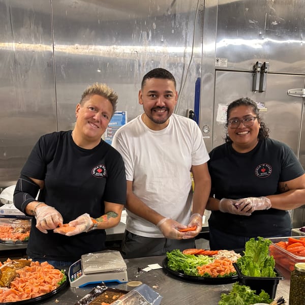 Three New York Bagels 'N Bialys employees preparing bagel toppings like lox, lettuce, and tomatoes.