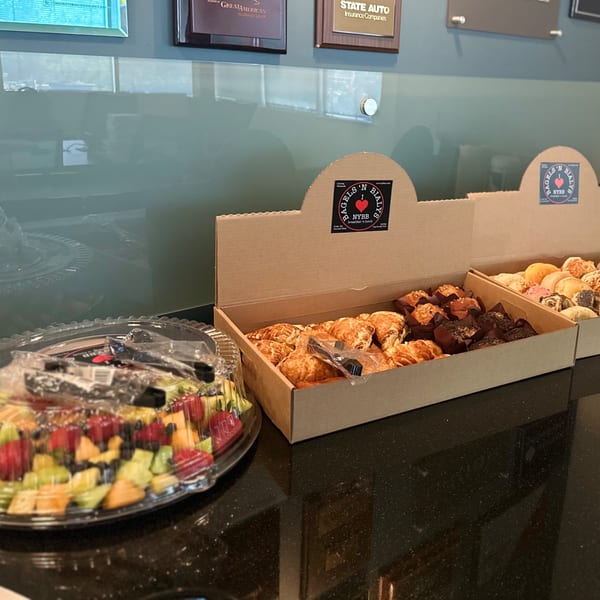 New York Bagels 'N Bialys boxes filled with pastries, muffins, and bagels, alongside a fruit platter.
