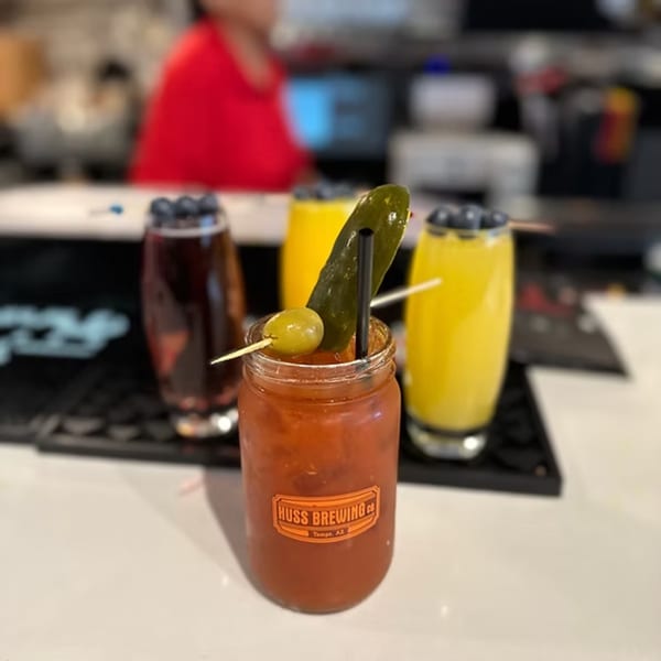 A Bloody Mary in a mason jar with a pickle and olive, alongside two blueberry-garnished drinks.