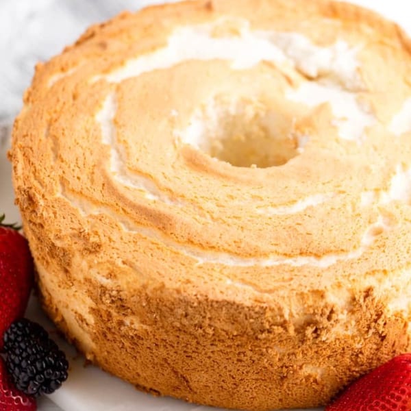 Golden-brown angel food cake with a hole in the center, garnished with fresh strawberries and blackberries.