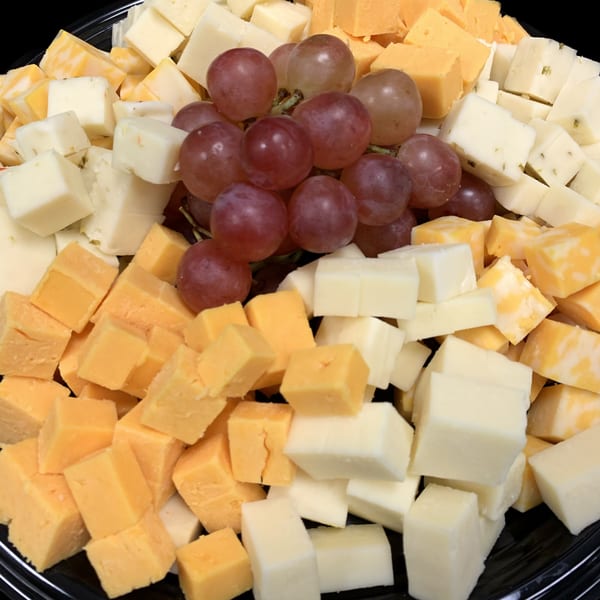 A platter of cubed cheeses, including cheddar and white varieties, with a cluster of red grapes.