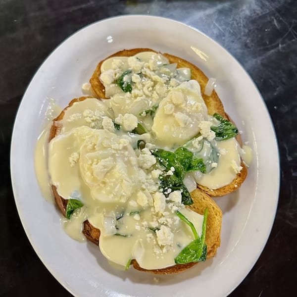 Two pieces of toast topped with poached eggs, creamy sauce, spinach, and crumbled cheese.